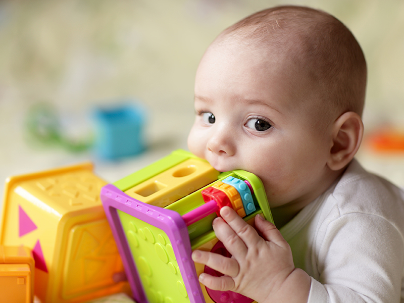 Baby putting a plastic toy in his mouth.